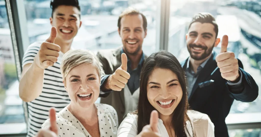 A diverse team of smiling professionals giving thumbs up to represent the success found when you understand why customer relationship is important.